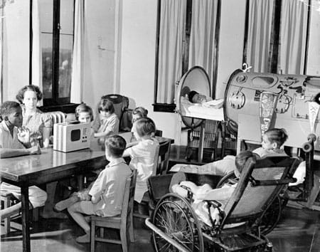 Boy in iron lung joins other children in playroom.